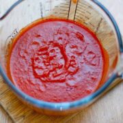 Tomato sauce in a glass measuring jug on a wooden surface.