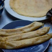 Three rolled- up pancakes sprinkled with sugar on a blue plate,