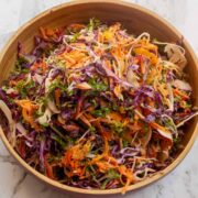 Finely shredded colourful vegetables in a wooden bowl on a marble worktop.