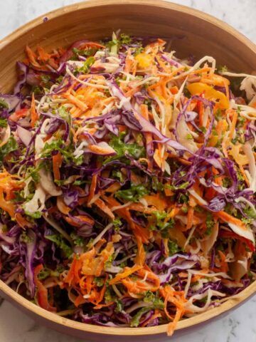 Finely shredded colourful vegetables in a wooden bowl on a marble worktop.