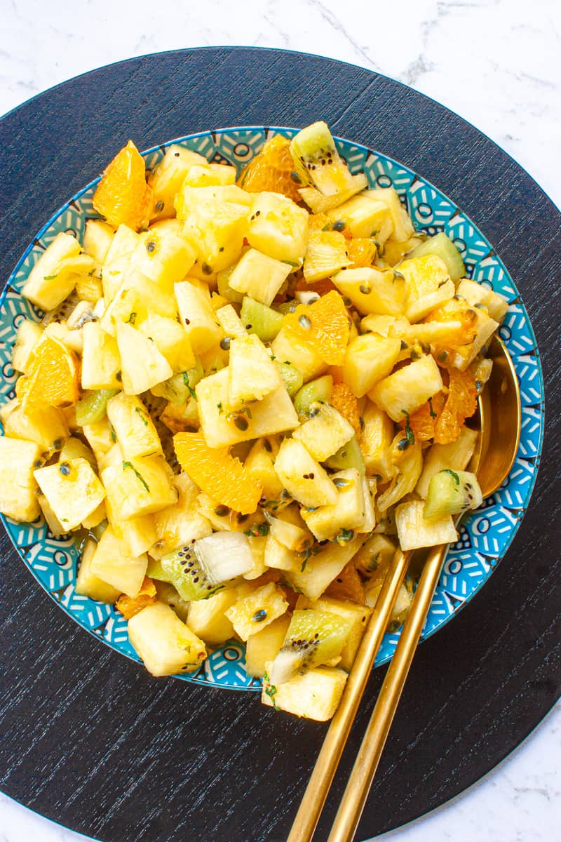 Fruit salad piled high in a blue bowl set on a black wooden placemat.