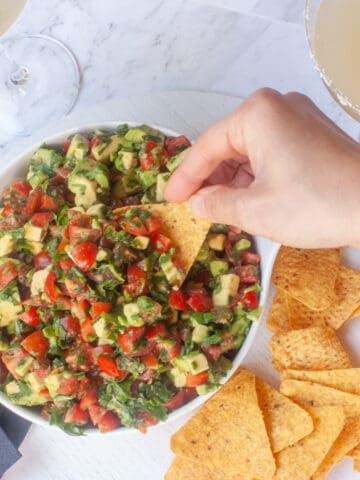 A hand scooping up the avo corn chip topper with a corn chip.