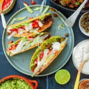 Three filled hard taco shells on a plate surrounded by the fillings.