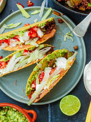 Three filled hard taco shells on a plate surrounded by the fillings.