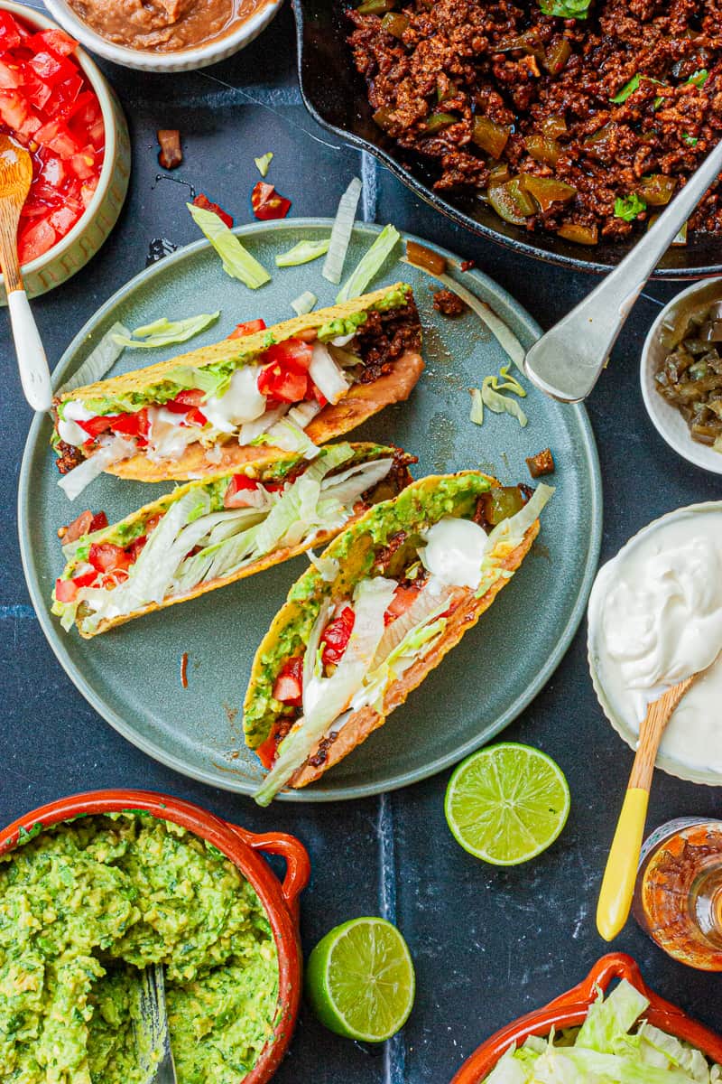 Three filled hard taco shells on a plate surrounded by the fillings.