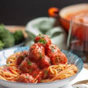 A generous pile of mini meatballs in tomato sauce on spaghetti in a blue bowl.