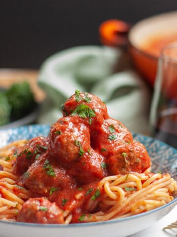 A generous pile of mini meatballs in tomato sauce on spaghetti in a blue bowl.