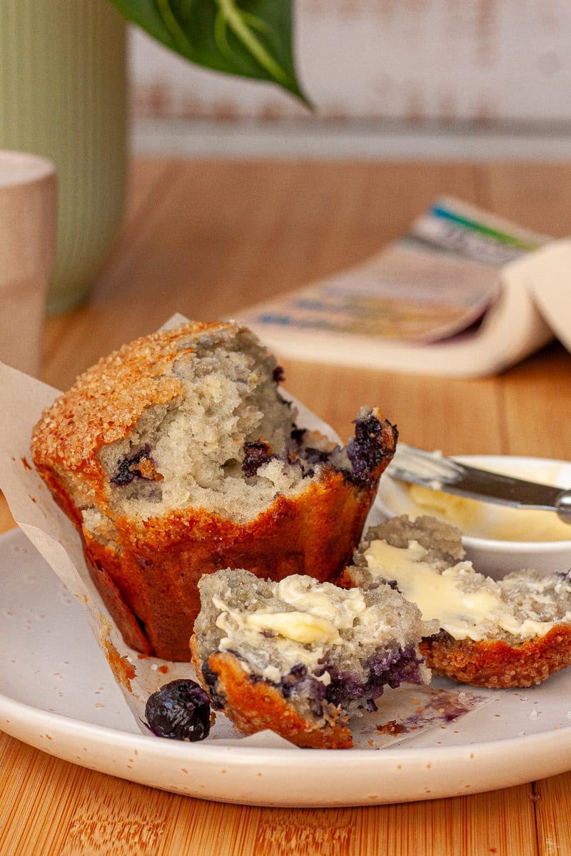 Close-up of a blueberry muffin. A chunk torn off and slathered with butter.