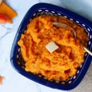 Square blue bowl containing orange mashed veg with a square of melting butter on the top.