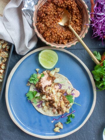 Street taco loaded with mini roasted cauliflower florets and other fillings on a bright blue plate.