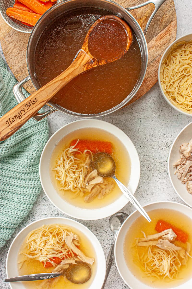 Looking down into a bowls of clear yellow broth with fine noodles, carrot and shredded chicken.