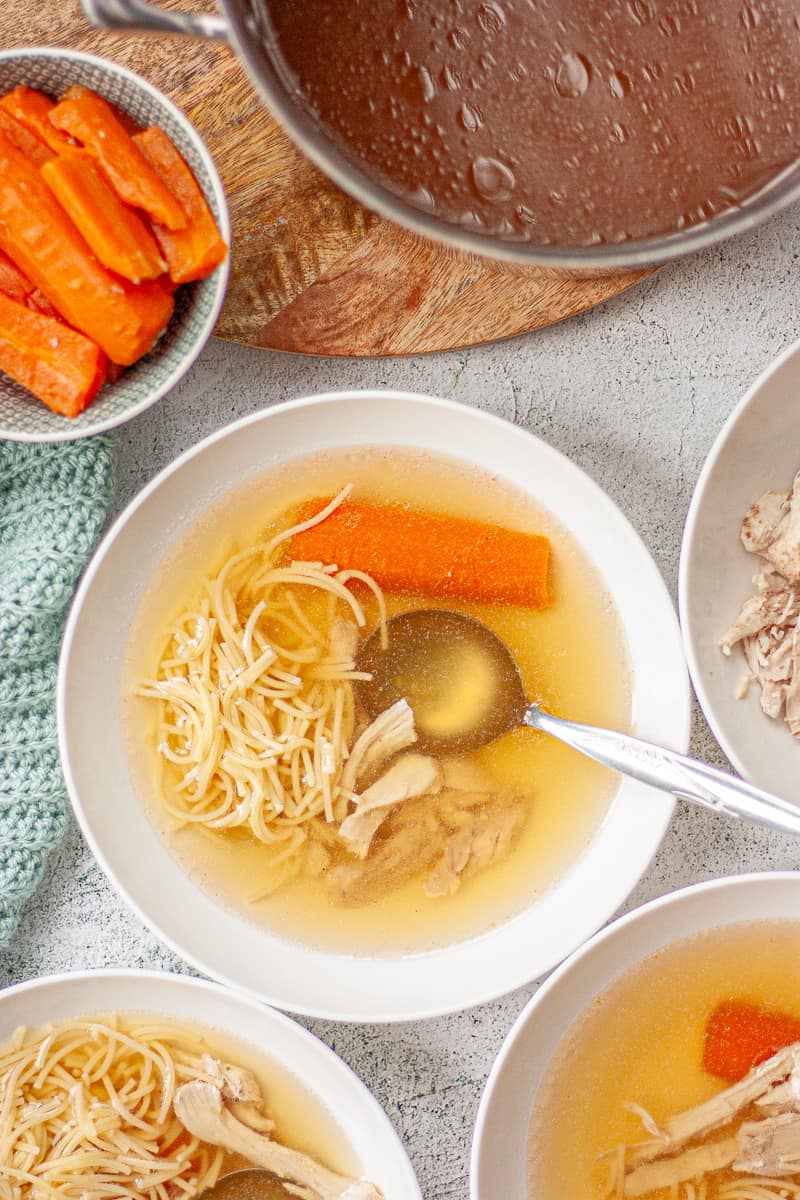 Looking down into bowls of clear yellow broth with fine noodles, carrot and shredded chicken.