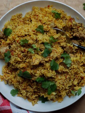 Bird's eye view of the finished pilau on a big white platter scattered with coriander leaves.