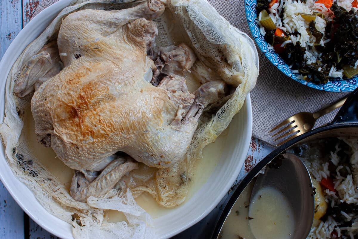 A whole braised chicken nestled in cheesecloth in a white bowl.