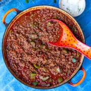 Bird's eye view of a large wide pot of chilli con carne on a blue tiled surface.