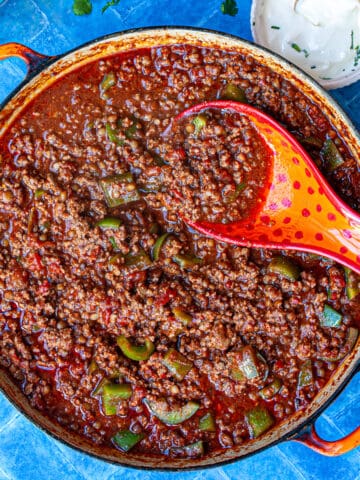 Bird's eye view of a large wide pot of chilli con carne on a blue tiled surface.