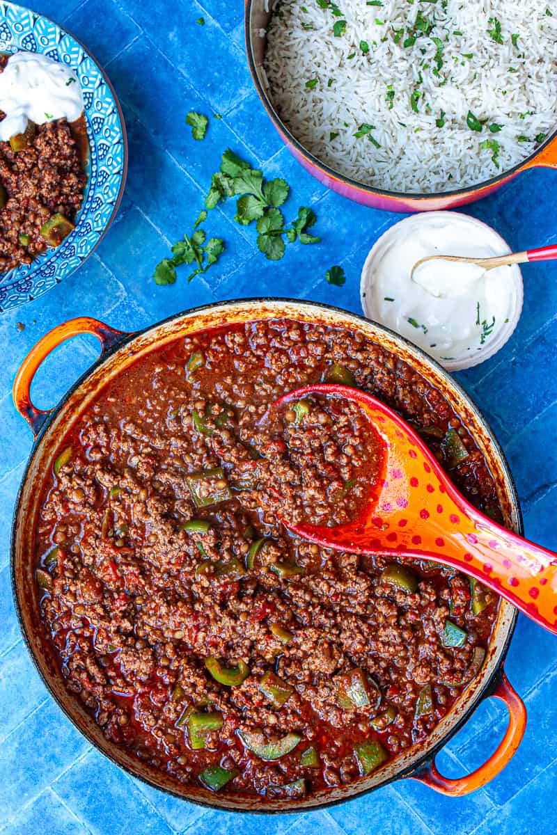 Bird's eye view of a large wide pot of chilli con carne on a blue tiled surface.