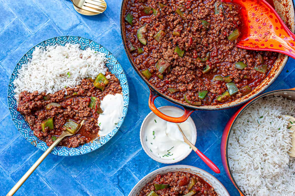 Portions of chilli served with rice set on a blue tiled background.