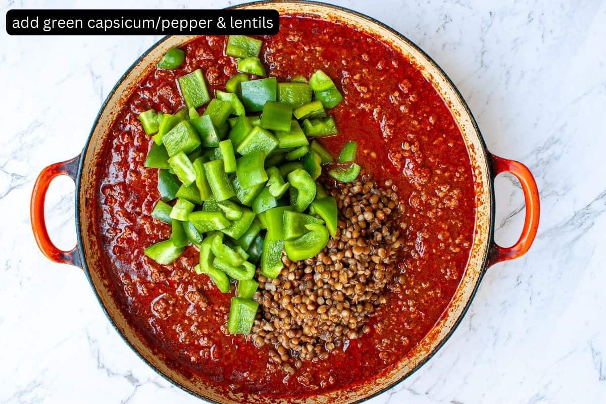 Top view of chilli in a large wide pan. Cubes of green capsicum and canned lentils have just been added.