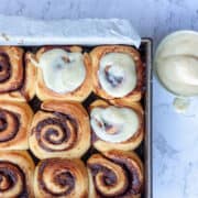 Top view of a tray of cinnamon buns. Some are topped with cream cheese icing.