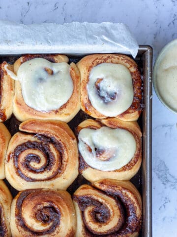 Top view of a tray of cinnamon buns. Some are topped with cream cheese icing.