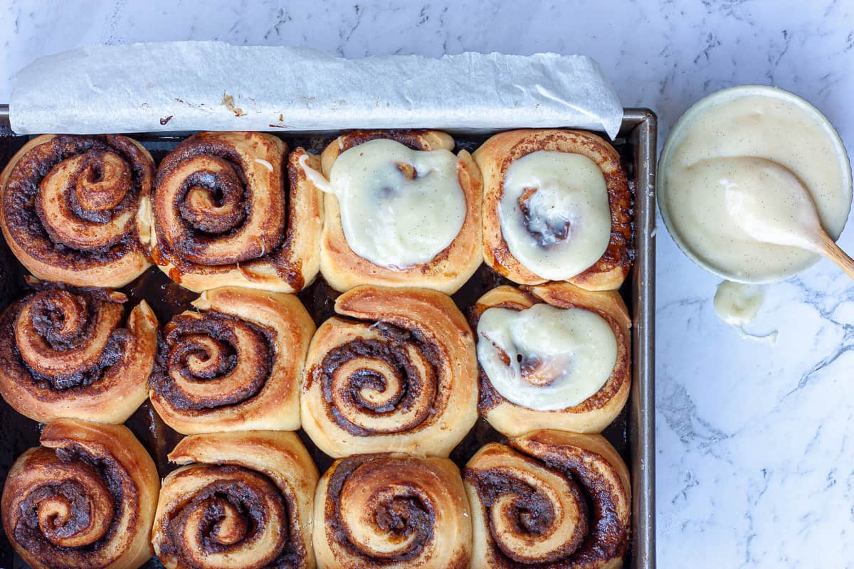 Top view of a tray of cinnamon buns. Some are topped with cream cheese icing.