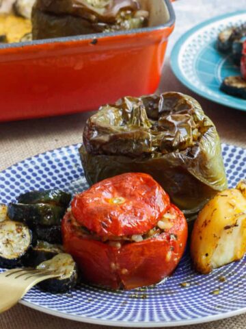 Stuffed tomato and capsicum with potato chunks and zucchini discs on a blue patterned plate.