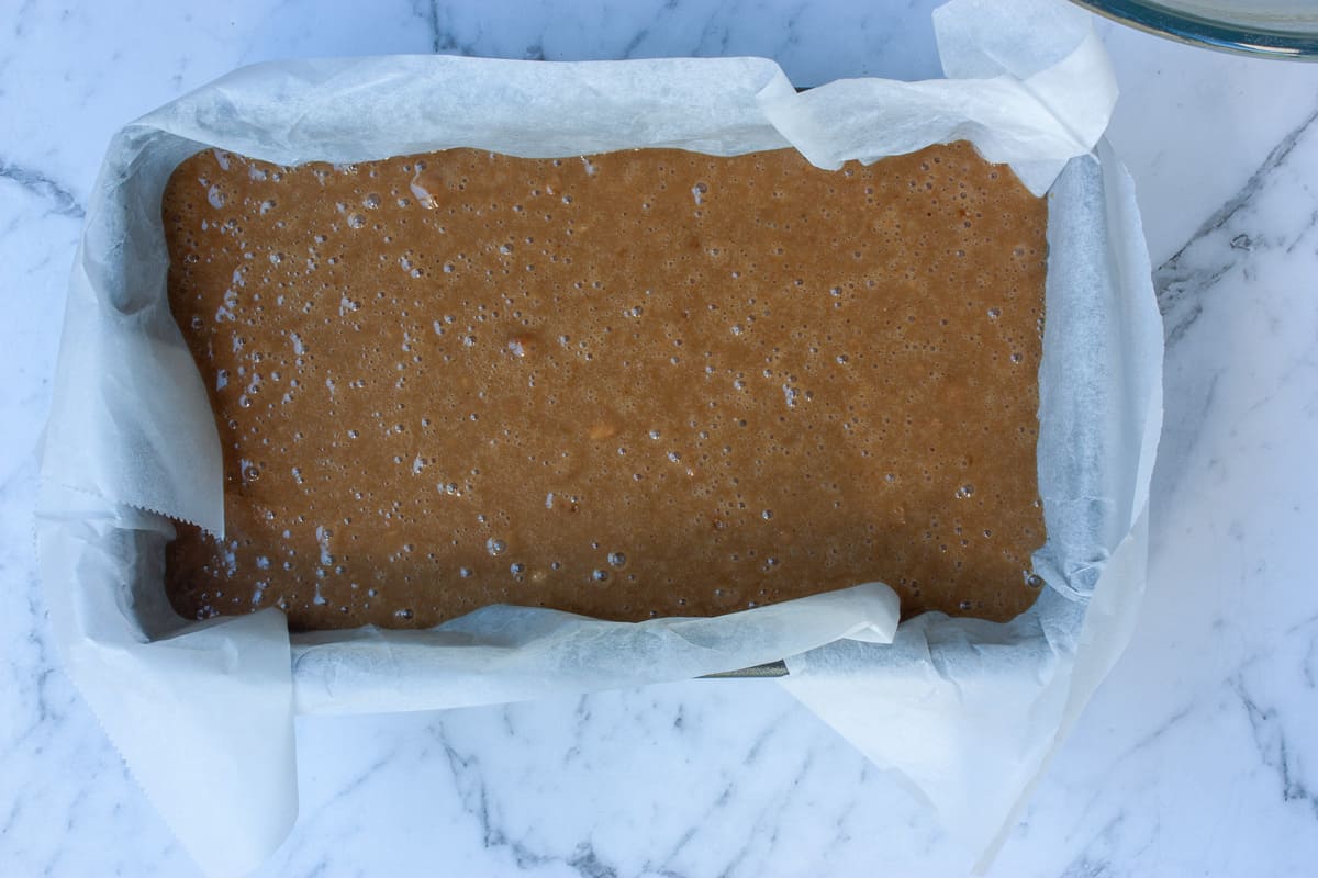 Raw brown batter covered with tiny bubbles in a lined loaf pan.