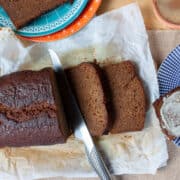 Partly sliced ginger loaf cake. A heavily buttered slice on a blue plate with a bite taken out of a corner.