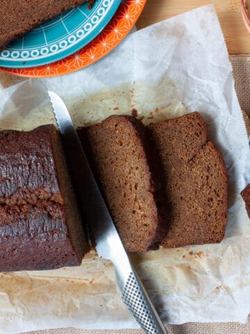 Partly sliced ginger loaf cake. A heavily buttered slice on a blue plate with a bite taken out of a corner.