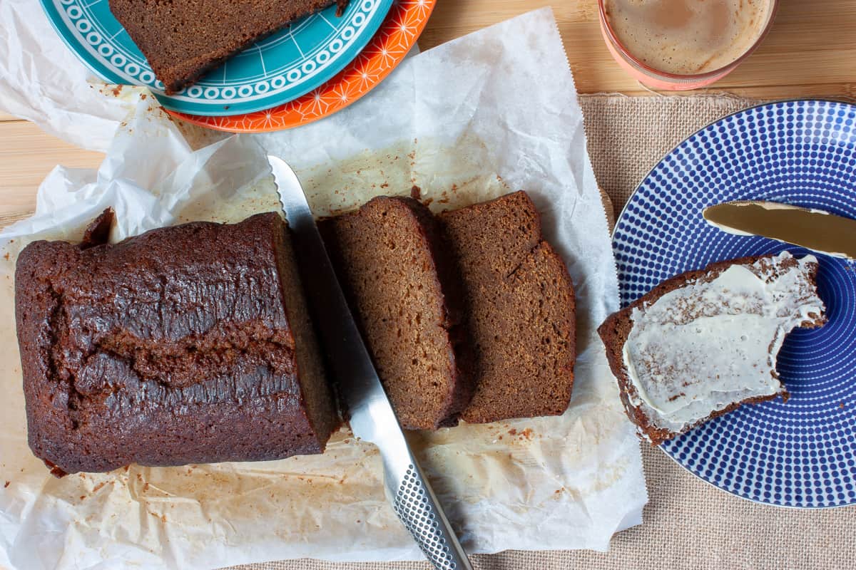 Partly sliced ginger loaf cake. A heavily buttered slice on a blue plate with a bite taken out of a corner.