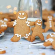 Happy gingerbread people propped up against a small glass bottle of milk. Other biscuits around them.