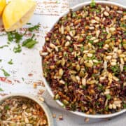 Grain salad in a white bowl with a small dish of toasted seeds to the side.