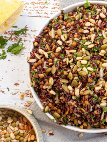 Grain salad in a white bowl with a small dish of toasted seeds to the side.