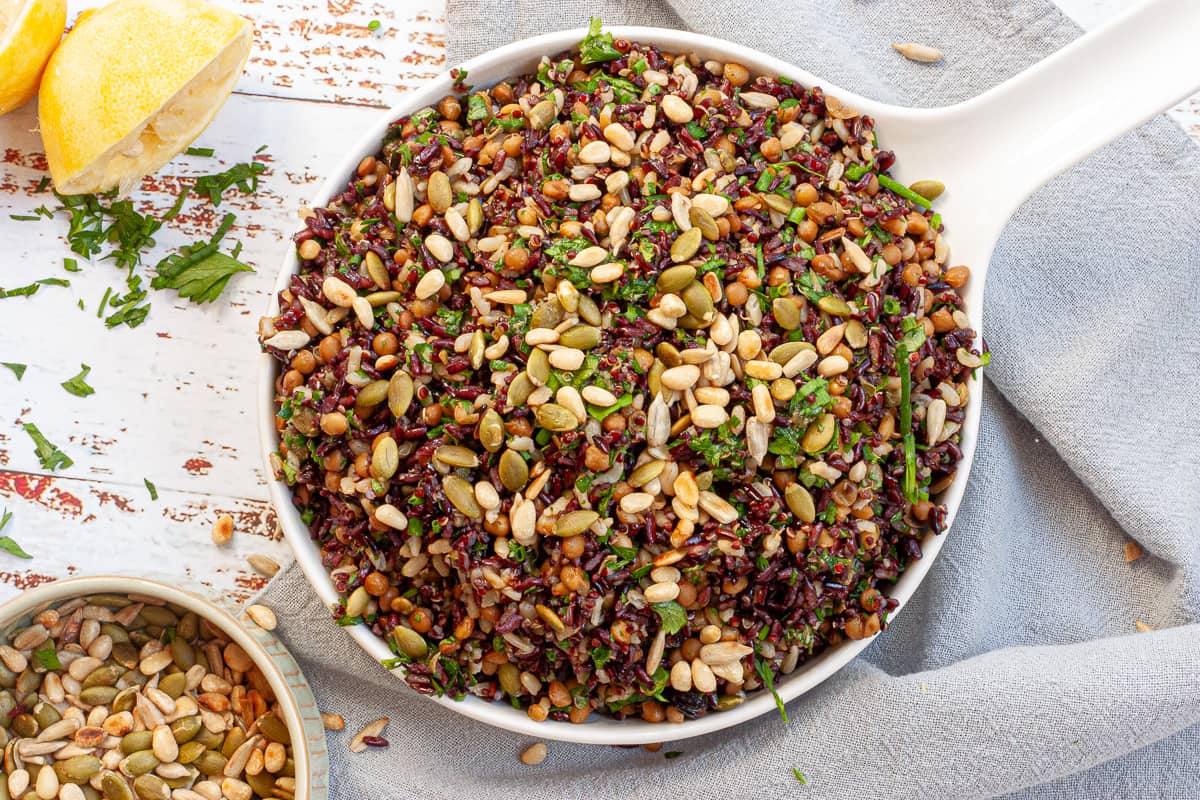 Big white bowl full of grain salad. Toasted seeds in a small bowl nearby.