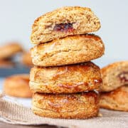 A stack of bronzed scones. The top one is cut in half to reveal a jammy centre.