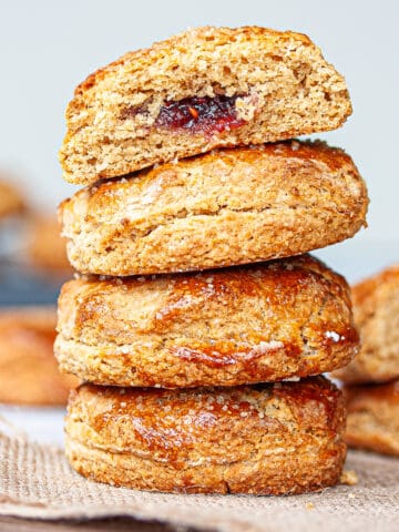 A stack of bronzed scones. The top one is cut in half to reveal a jammy centre.