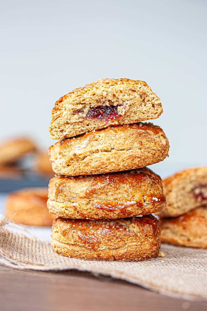 A stack of bronzed scones. The top one is cut in half to reveal a jammy centre.