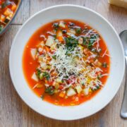 Overhead view of a bowl of soup in a white bowl set on a wooden surface. Grated parmesan scattered over the top.