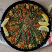 Paella in a pan scattered with chopped fresh parsley and lemon wedges.