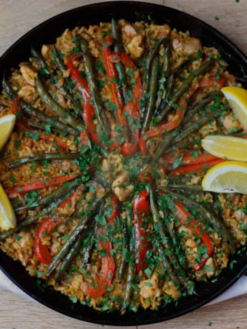 Paella in a pan scattered with chopped fresh parsley and lemon wedges.