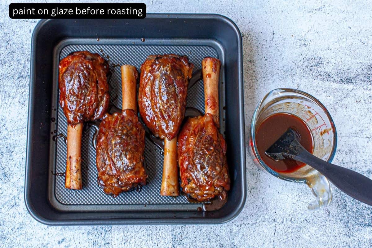 Lamb shanks in a roasting pan glazed with a glossy sauce.