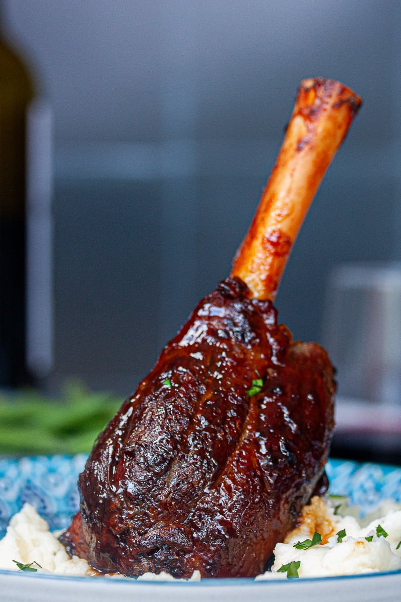 A single glossy bronzed lamb shank sitting upright in a bed of mashed potato.