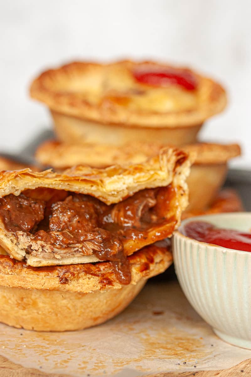 Stacked individual meat pies. One is cut in half and the filling is oozing out slightly.