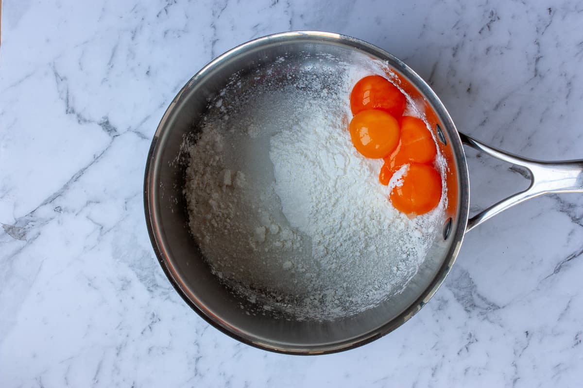 Top view of whole egg yolks in a saucepan with white powder (sugar, cornflour & salt).