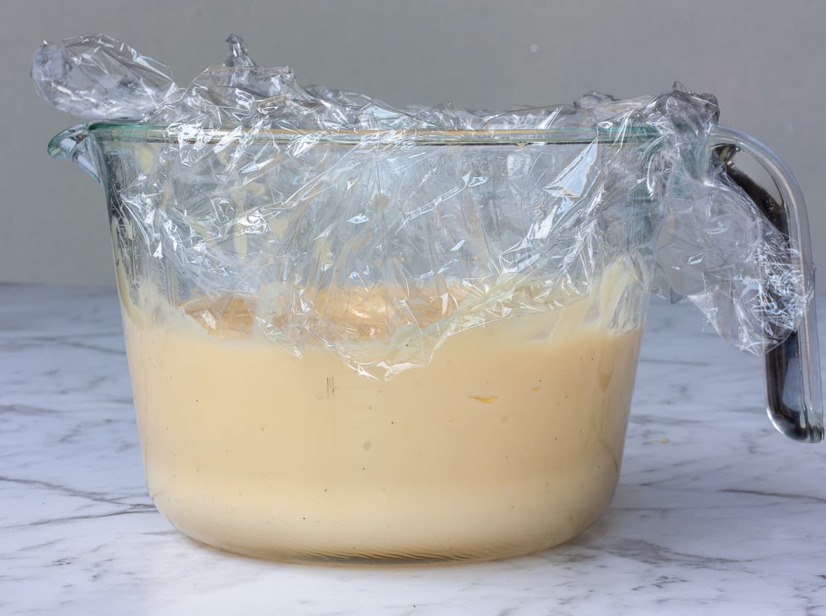 Custard in a glass measuring jug closely covered in plastic wrap.