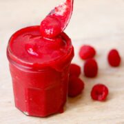 teaspoon dipping in a over-filled jam jar containing finished raspberry sauce. Some sauce dripping down the side.