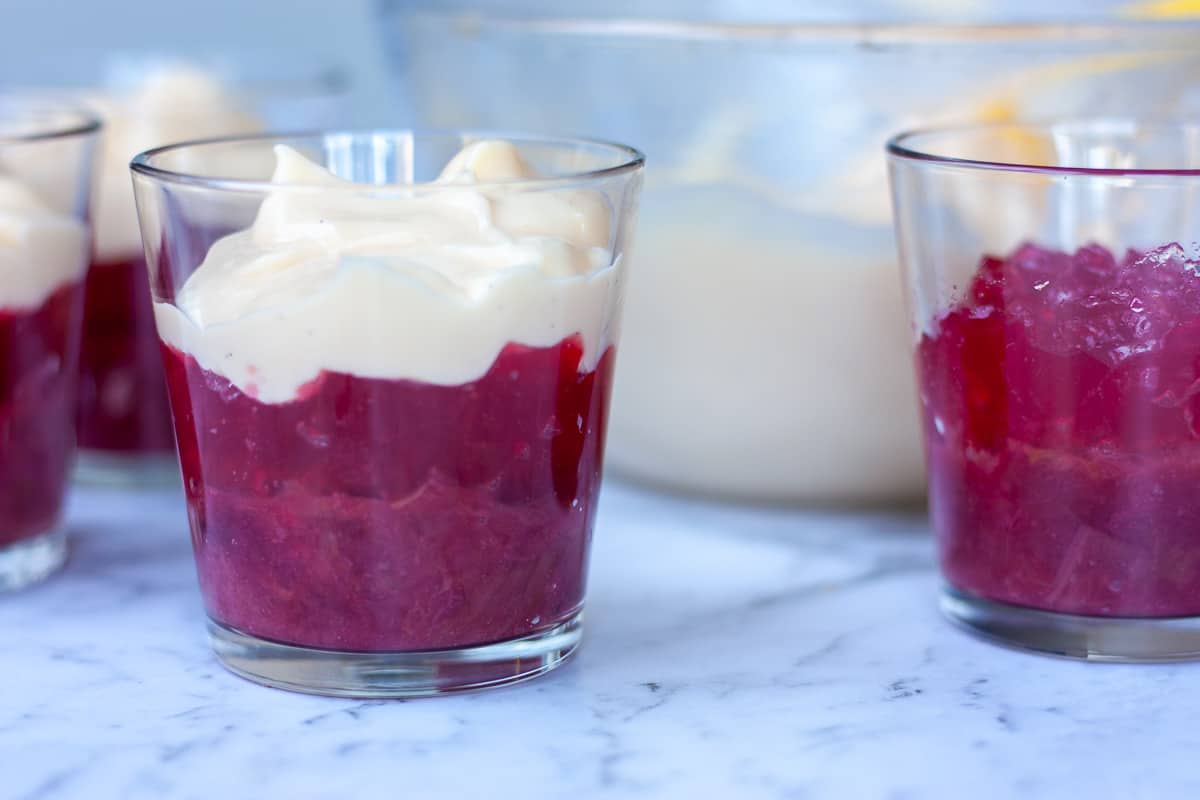 Side view of trifle glasses showing custard layer atop rhubarb-coloured layers.