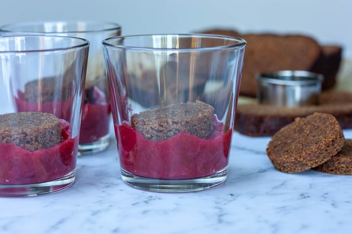 Side view of trifle glasses containing rounds of gingerbread cake atop rhubarb compote.