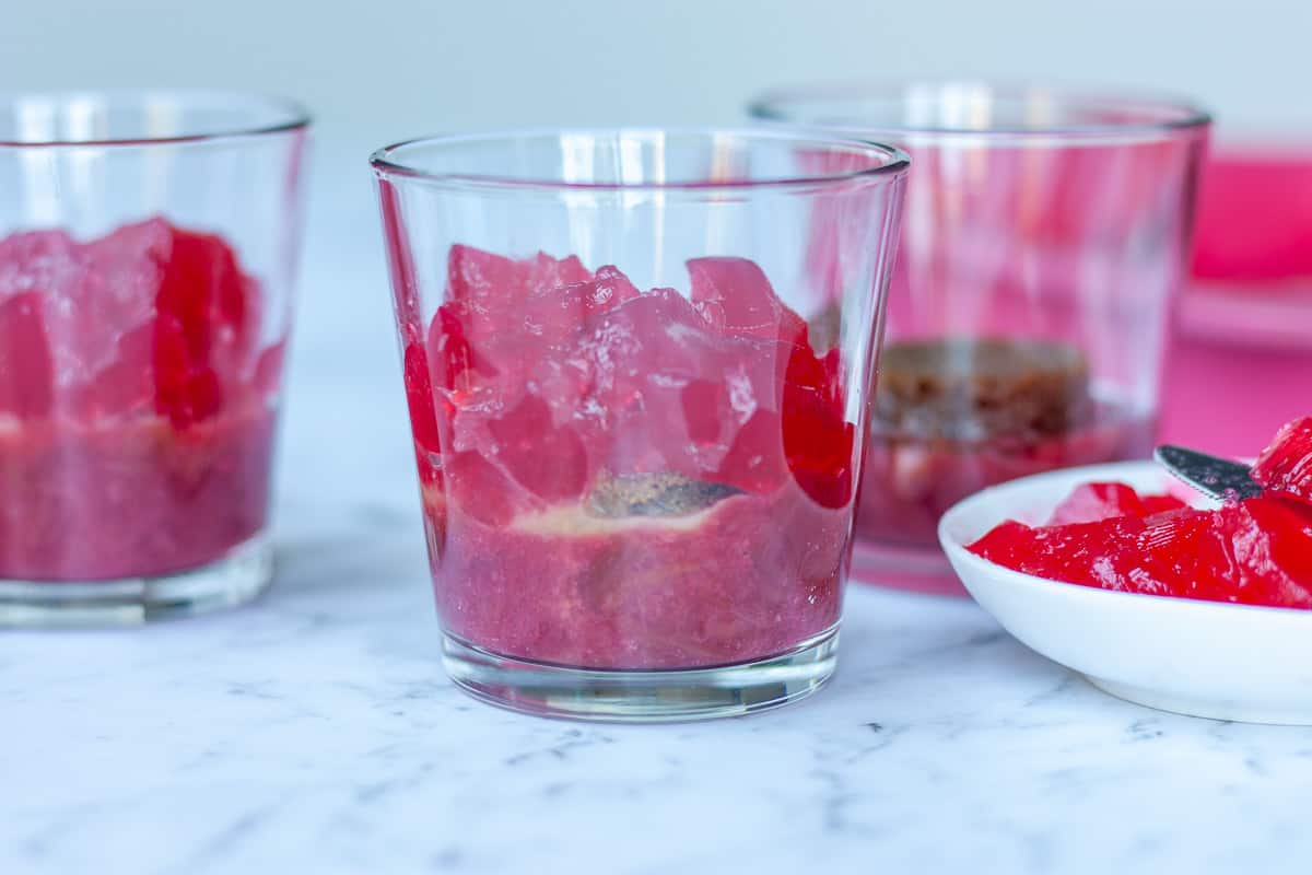 Side view of trifle glasses showing softly set rhubarb jelly layer being applied.